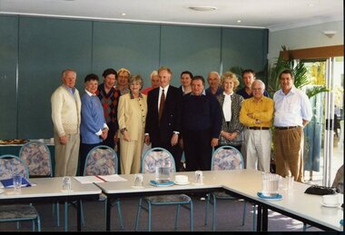 Group of people standing behind tables and chairs set in open rectangle layout