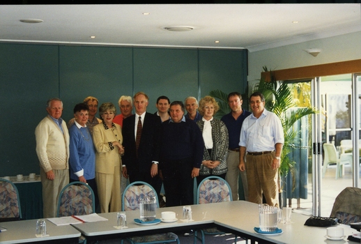 Group of people standing behind tables and chairs set in open rectangle layout