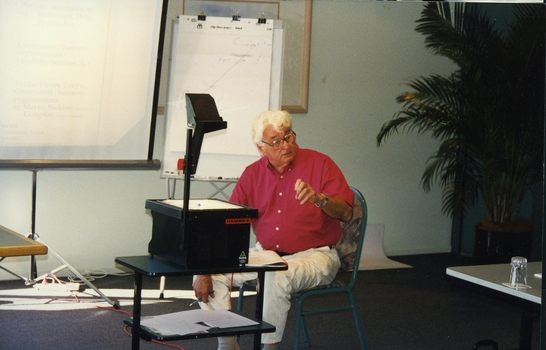 Man seated as he uses overhead projector