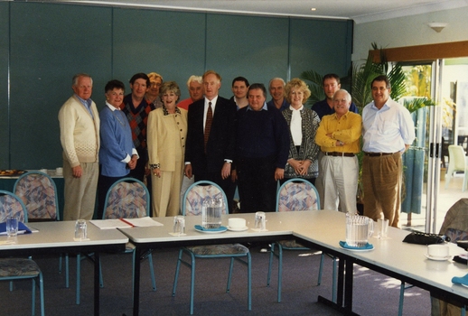 Group of people standing behind tables and chairs set in open rectangle layout