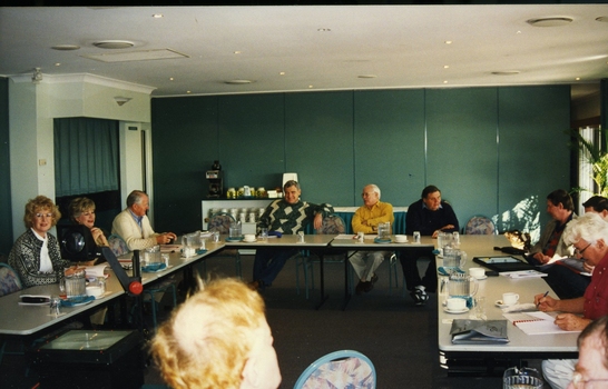 Group of people seated at tables set in open rectangle layout