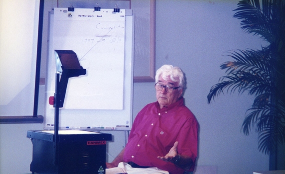Man seated as he uses an overhead projector
