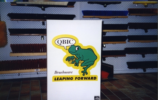 QBIC frog log in front of display rack of broom heads