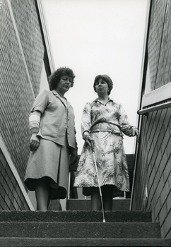 Female instructor speaks to woman with white cane as she descends the stairs