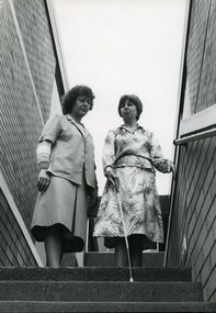 Female instructor speaks to woman with white cane as she descends the stairs