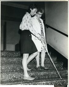 Barbara Giblin assists a client moving downstairs with a white cane