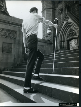 Man holds out long cane as he ascends church steps
