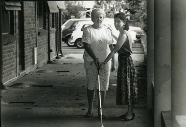 Woman touches shoulder and holds cane down for another who is about to walk towards camera