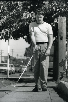 Man walks along suburban footpath with white cane