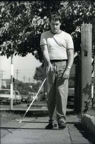 Man walks along suburban footpath with white cane