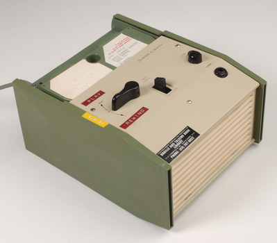 Green and cream box with black levers and removable plastic cartridge housing magnetic tape.