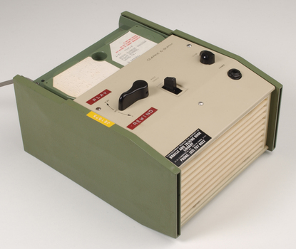 Green and cream box with black levers and removable plastic cartridge housing magnetic tape.