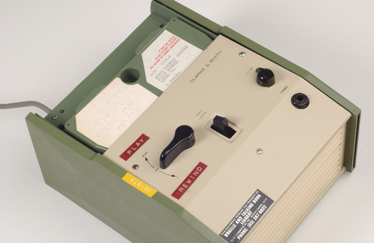 Green and cream box with black levers and removable plastic cartridge housing magnetic tape.