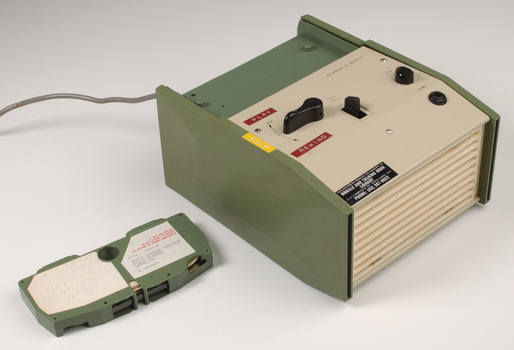 Green and cream box with black levers and removable plastic cartridge housing magnetic tape.