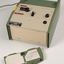 Green and cream box with black levers and removable plastic cartridge housing magnetic tape.