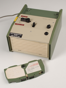 Green and cream box with black levers and removable plastic cartridge housing magnetic tape.