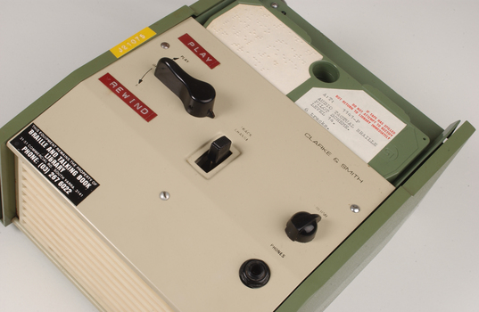 Green and cream box with black levers and removable plastic cartridge housing magnetic tape.