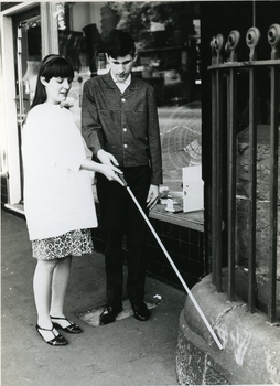 Woman raising white cane man is holding to make it touch a guttering