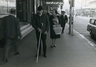 Man using white cane as he walks along busy city street