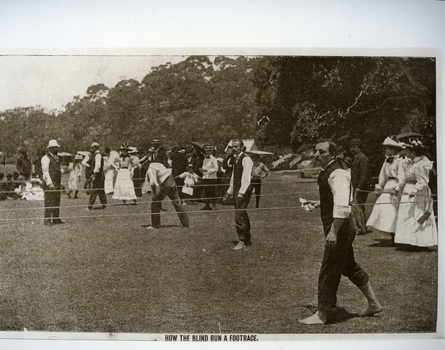 Men, without shoes, hold a string line whilst ladies in early 20th century dresses stand nearby