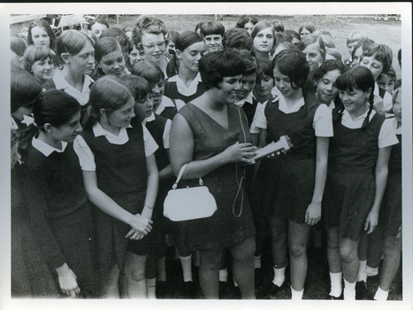 Woman uses an electronic device surrounded by schoolgirls