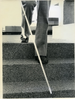 Bottom half of male walking down steps at Enfield using a white cane