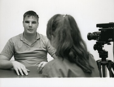 Man speaking to a woman whilst a video camera is directed at him