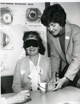 One woman helps another find her cup of tea whilst wearing a blindfold