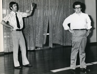 Two men stand on stage facing towards an audience