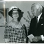 Kitty Rose and Sir Rohan Delacombe stand next to a portrait of Queen Elizabeth II