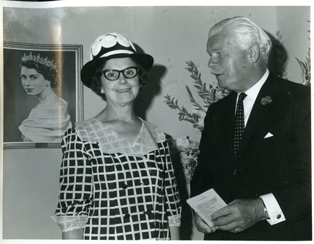 Kitty Rose and Sir Rohan Delacombe stand next to a portrait of Queen Elizabeth II