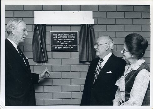 John Wicking holds cord opening curtain across plaque with Kitty Rose and John Wilson looking on