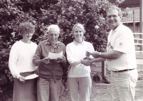 Man shakes hands with a woman as he hands her a piece of paper, with two others having already received theirs