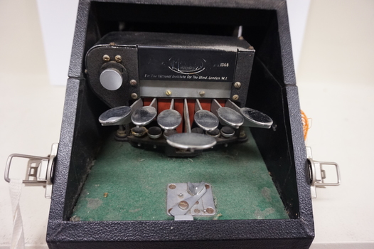 Seven silver oval keys attached to black vinyl covered device inside black box
