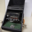 Seven silver oval keys attached to black vinyl covered device inside black box