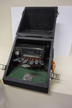 Seven silver oval keys attached to black vinyl covered device inside black box