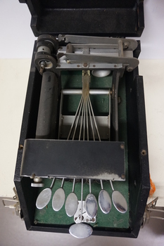 Seven silver oval keys attached to black vinyl covered device inside black box