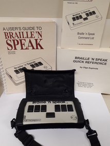 Braille'n'Speak device surrounded by printed and Braille manual and command list