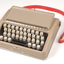 Tan case with flip top lid exposing keyboard, and red handle strap
