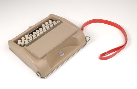 Tan case with flip top lid exposing keyboard, and red handle strap
