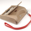 Tan case with flip top lid exposing keyboard, and red handle strap