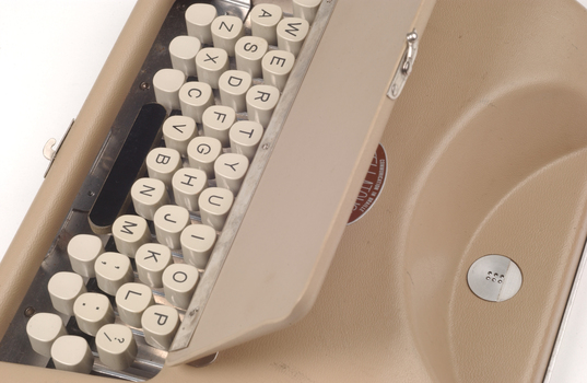 Tan case with flip top lid exposing keyboard, and red handle strap