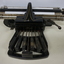 Black rectangular base with seven black keys and silver plates for producing Braille at rear