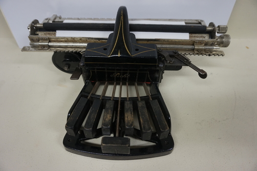 Black rectangular base with seven black keys and silver plates for producing Braille at rear