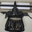 Black rectangular base with seven black keys and silver plates for producing Braille at rear