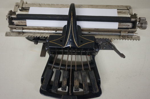 Black rectangular base with seven black keys and silver plates for producing Braille at rear