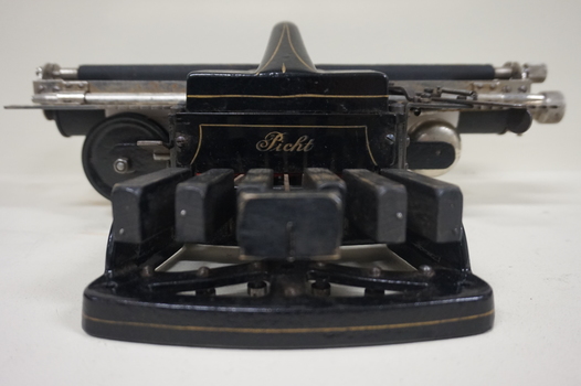 Black rectangular base with seven black keys and silver plates for producing Braille at rear