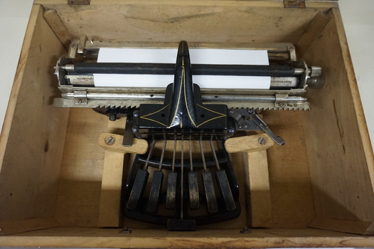 Black rectangular base with seven black keys and silver plates for producing Braille at rear