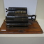 Black register shaped object on wooden board with metal levels and handles.