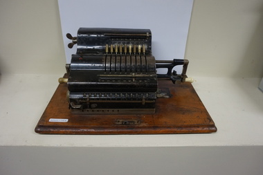 Black register shaped object on wooden board with metal levels and handles.